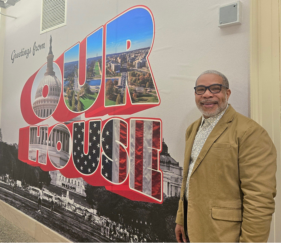 Michael Finnell standing in front of a wall mural that says "Greetings from Our House"