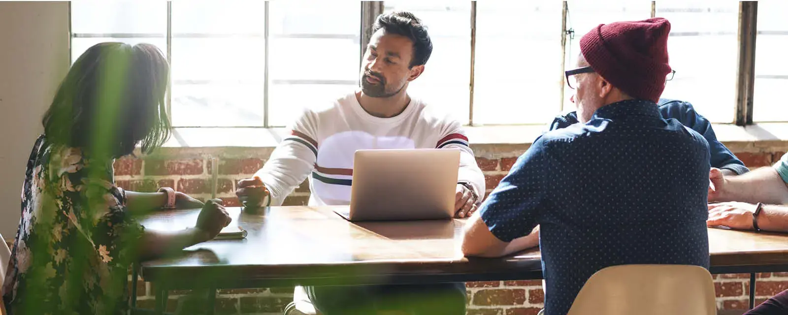 Diverse group of people having a meeting at table with a laptop. They are engaged in discussion, sitting in large windows room. Diverse people discussion at table in modern room. Meeting and discuss