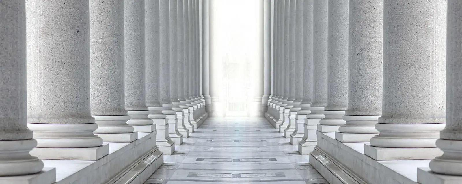 Two rows of white marble columns. Hallway with white pillars. Bright light between two rows of columns