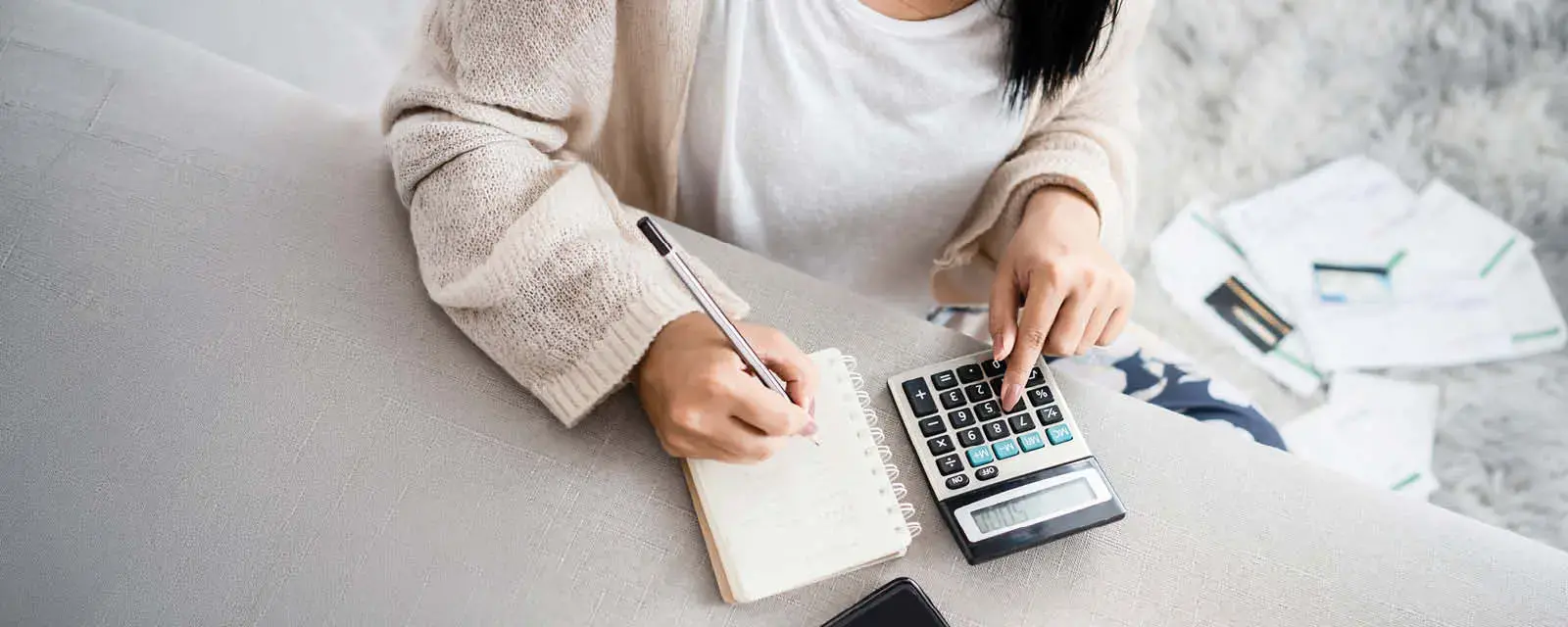 Close up of a one hand on a calculator, and the other hand taking notes in a notebook.