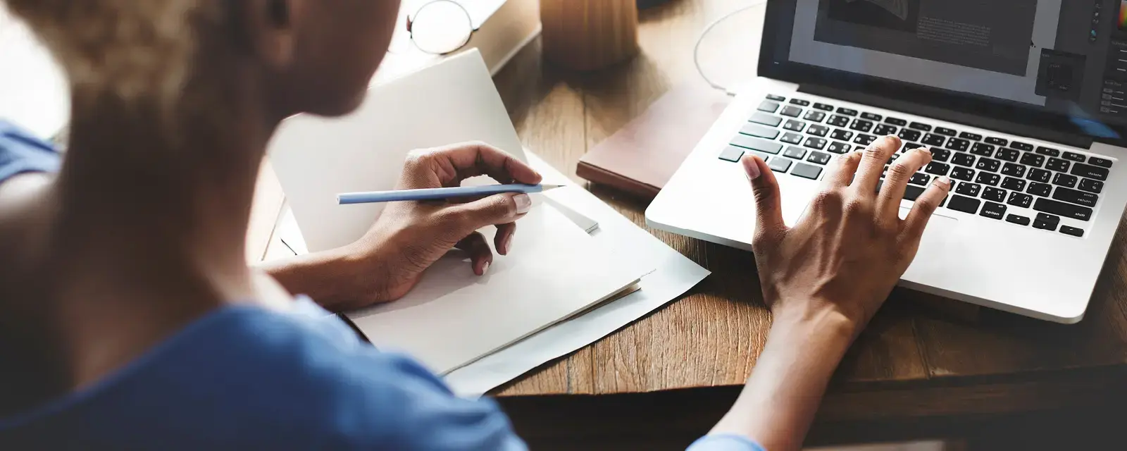 Close-up of a person at a computer, typing and taking notes
