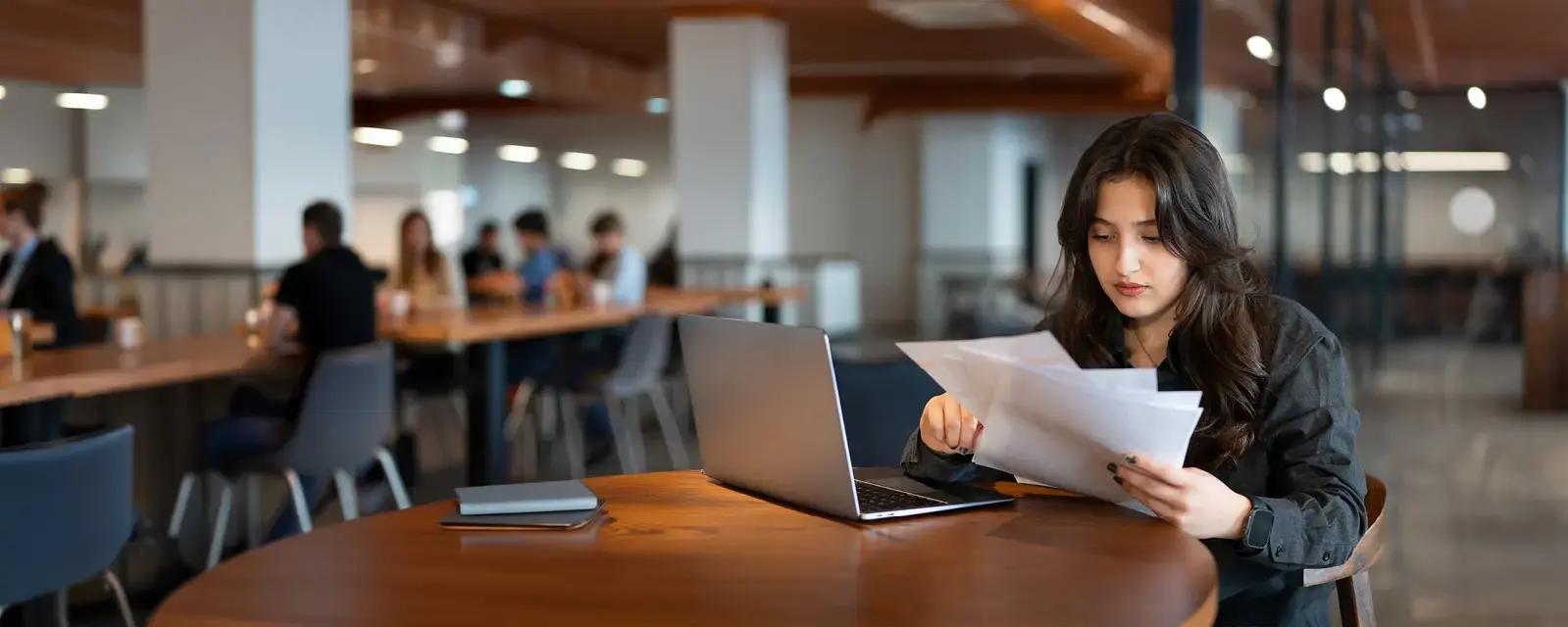 Young woman works with laptop in cafe and examines financial report papers.