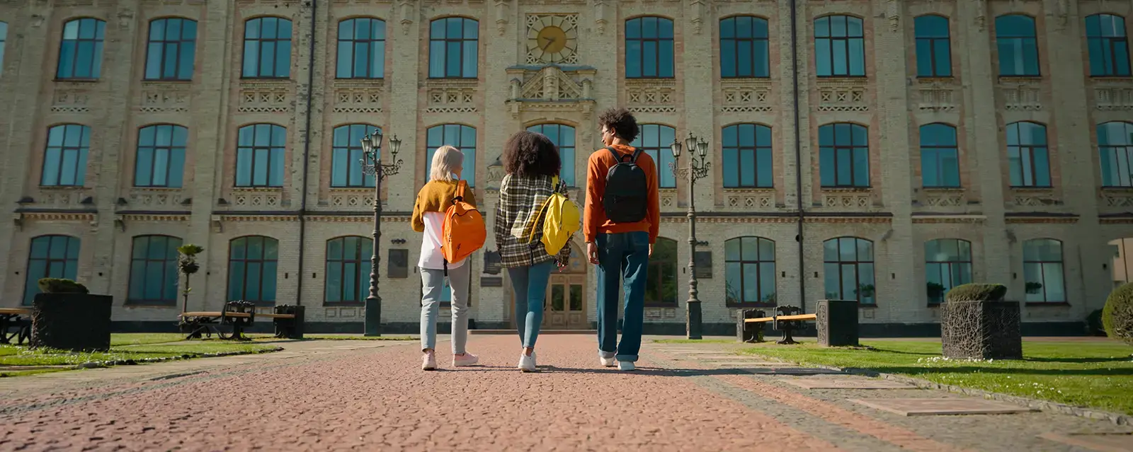 Back view of three people outside walking to class on a university campus. 