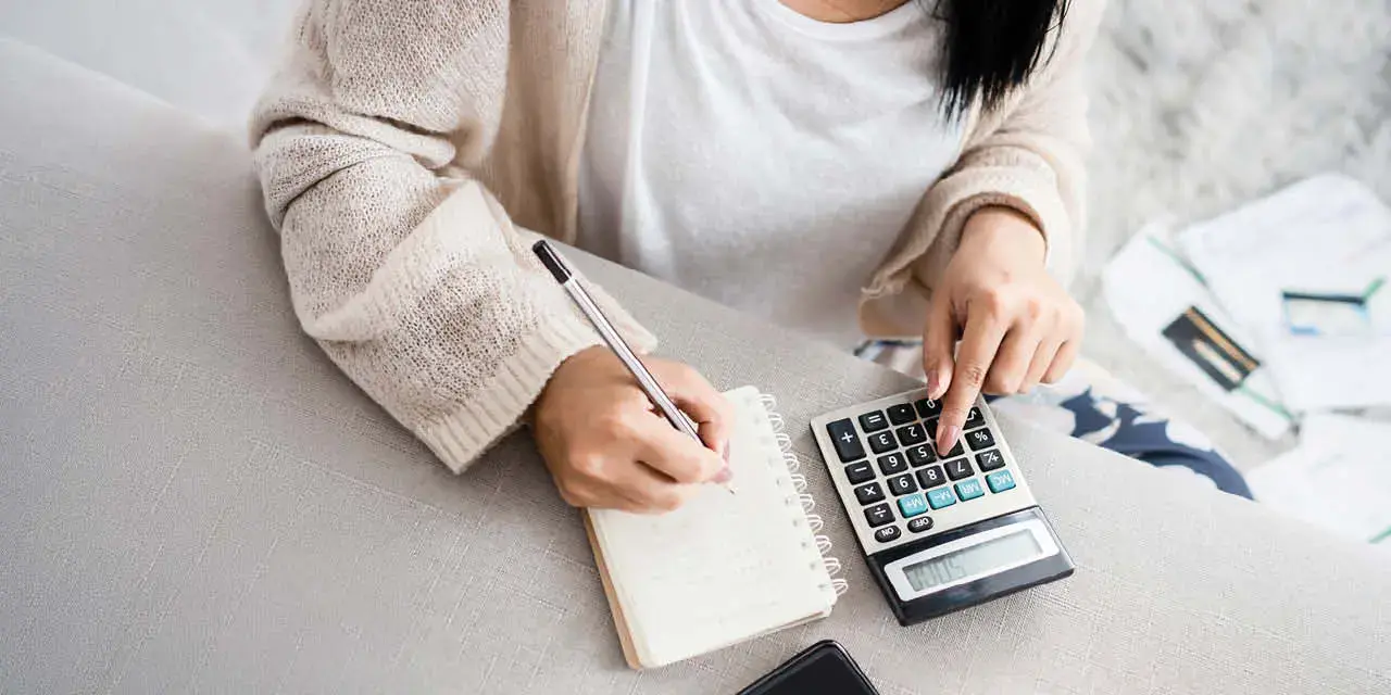 Close up of a one hand on a calculator, and the other hand taking notes in a notebook.