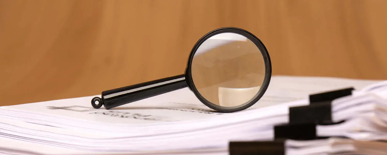 A magnifying glass rests on scattered clipped papers, symbolizing diligent research and careful analysis