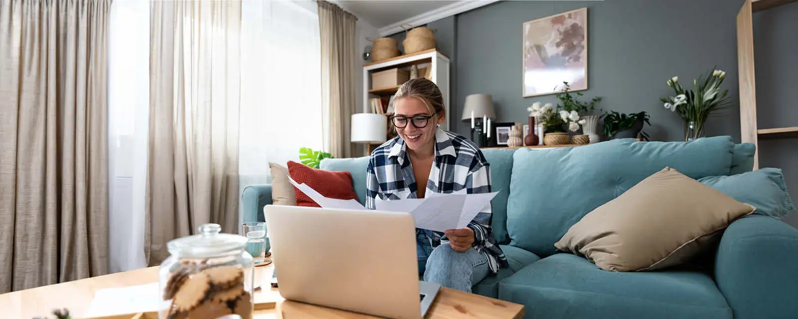 Female student holding papers in her hands and looking at a laptop.