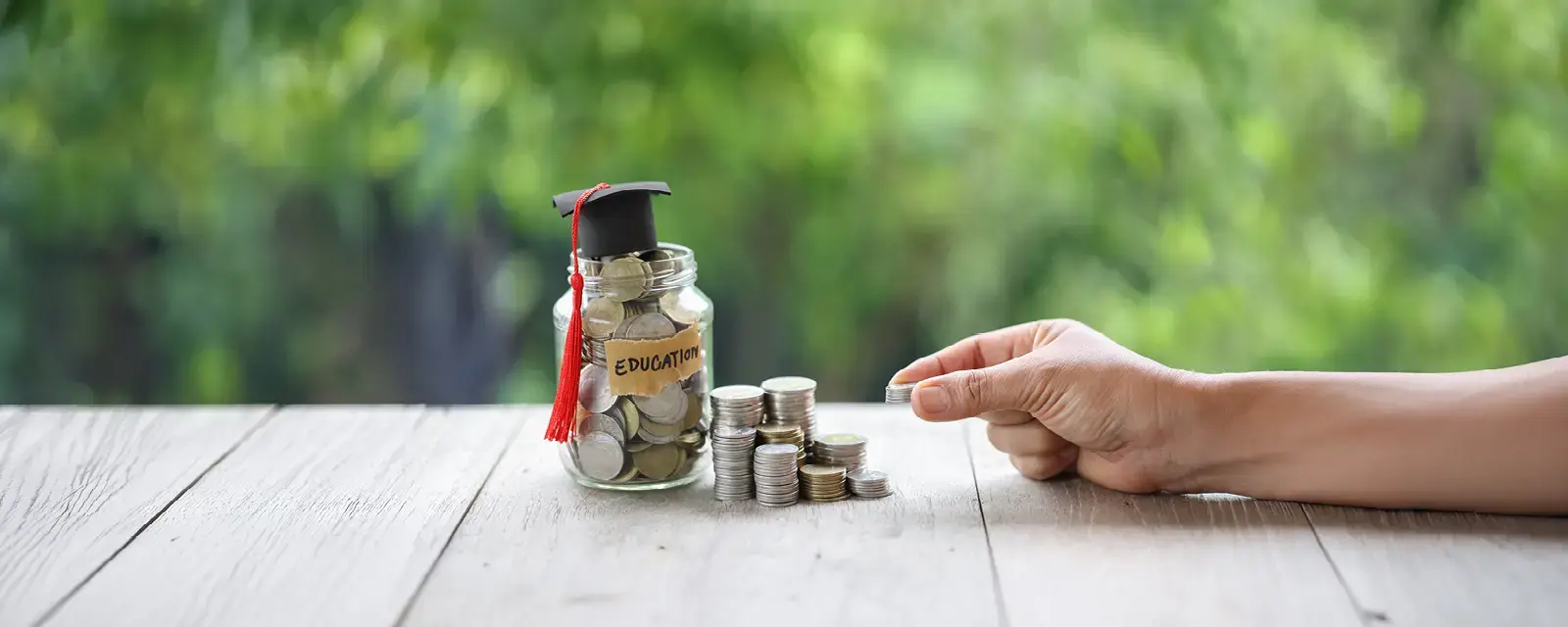 Stacks of coins next to a glass jar filled with coins labled 'Education'. There is a graduation cap on top of the jar.