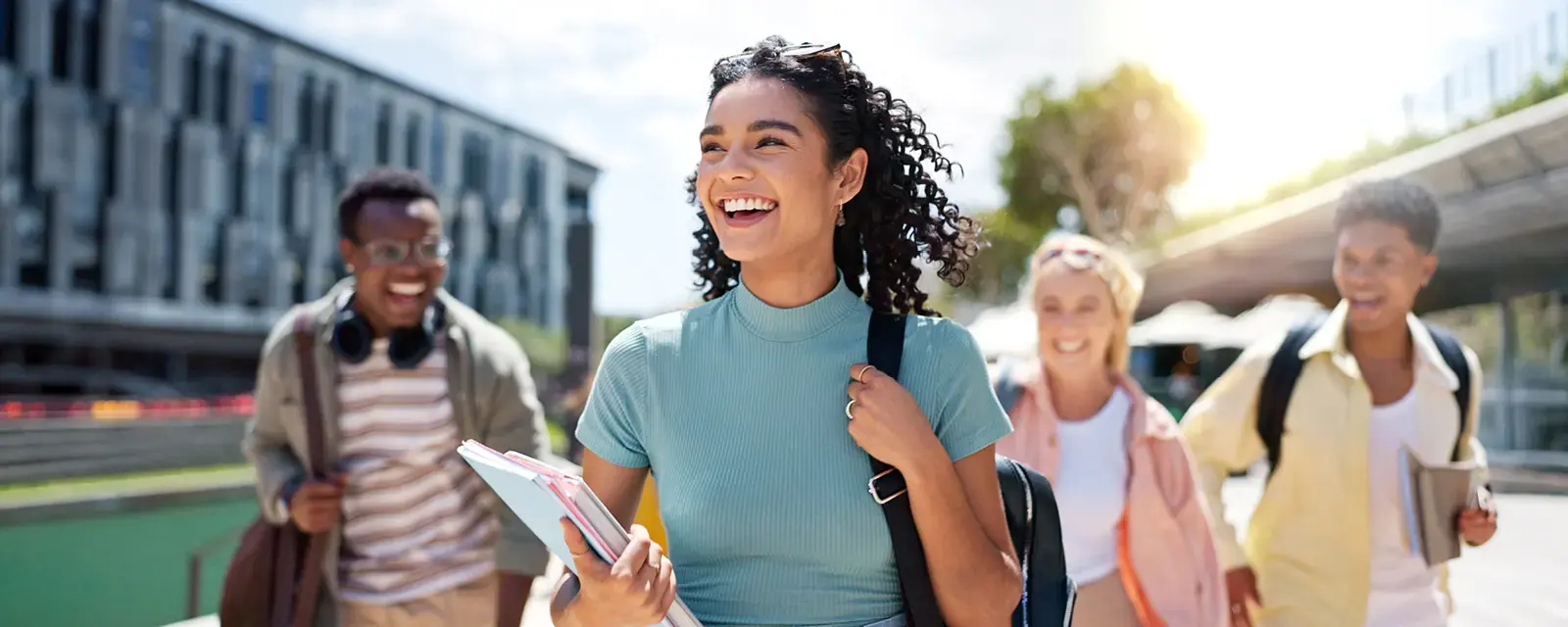 Smiling woman with a backpack over one shoulder and carrying text books.