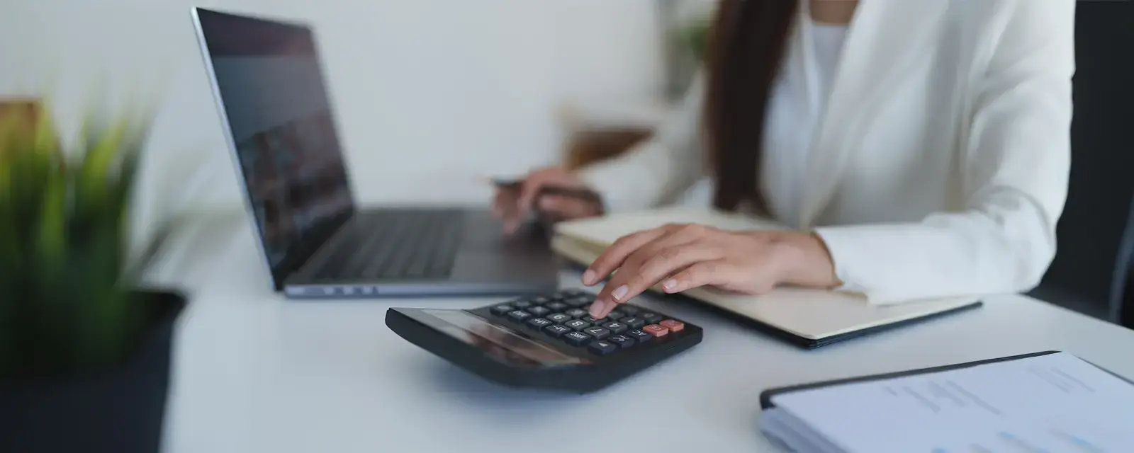Closeup of person at a desk with a laptop and calculator.