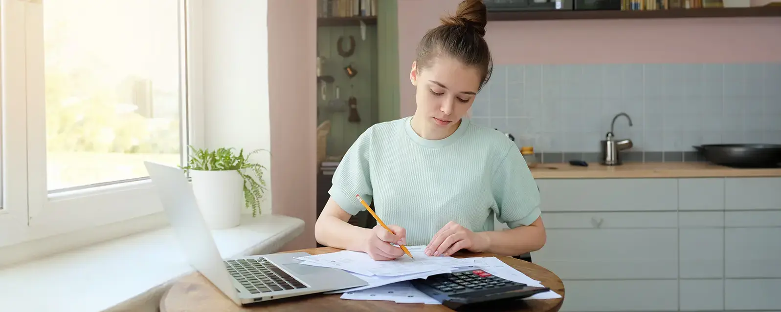 Portrait of young woman, sitting at kitchen table, filling out law school student loan application forms.
