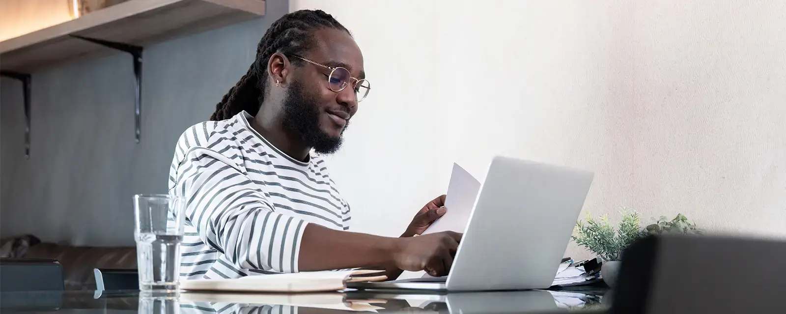 African American male law student working with laptop computer remote while sitting at glass table in living room.