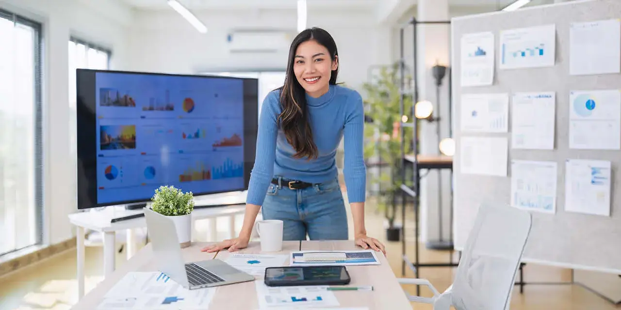Female leaning over a desk with financial charts and computer