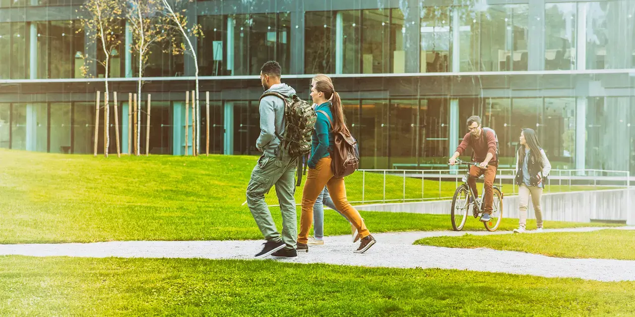 Two students with backpacks walking on a campus sidewalk.