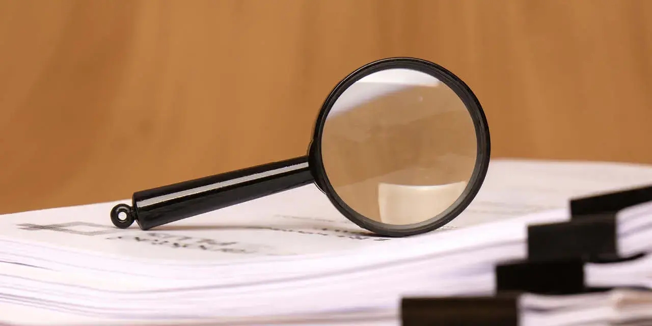 A magnifying glass rests on scattered clipped papers, symbolizing diligent research and careful analysis