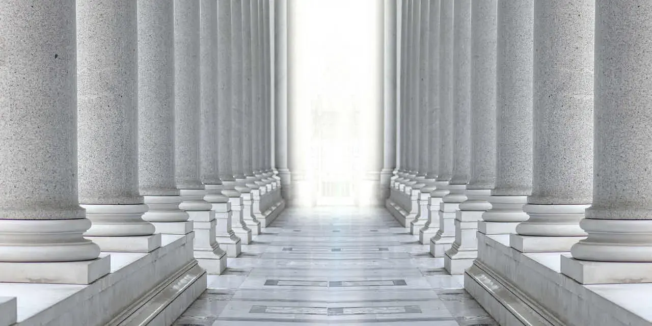 Two rows of white marble columns. Hallway with white pillars. Bright light between two rows of columns