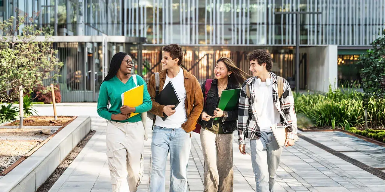 A diverse group of four students chatting as they walk across campus.