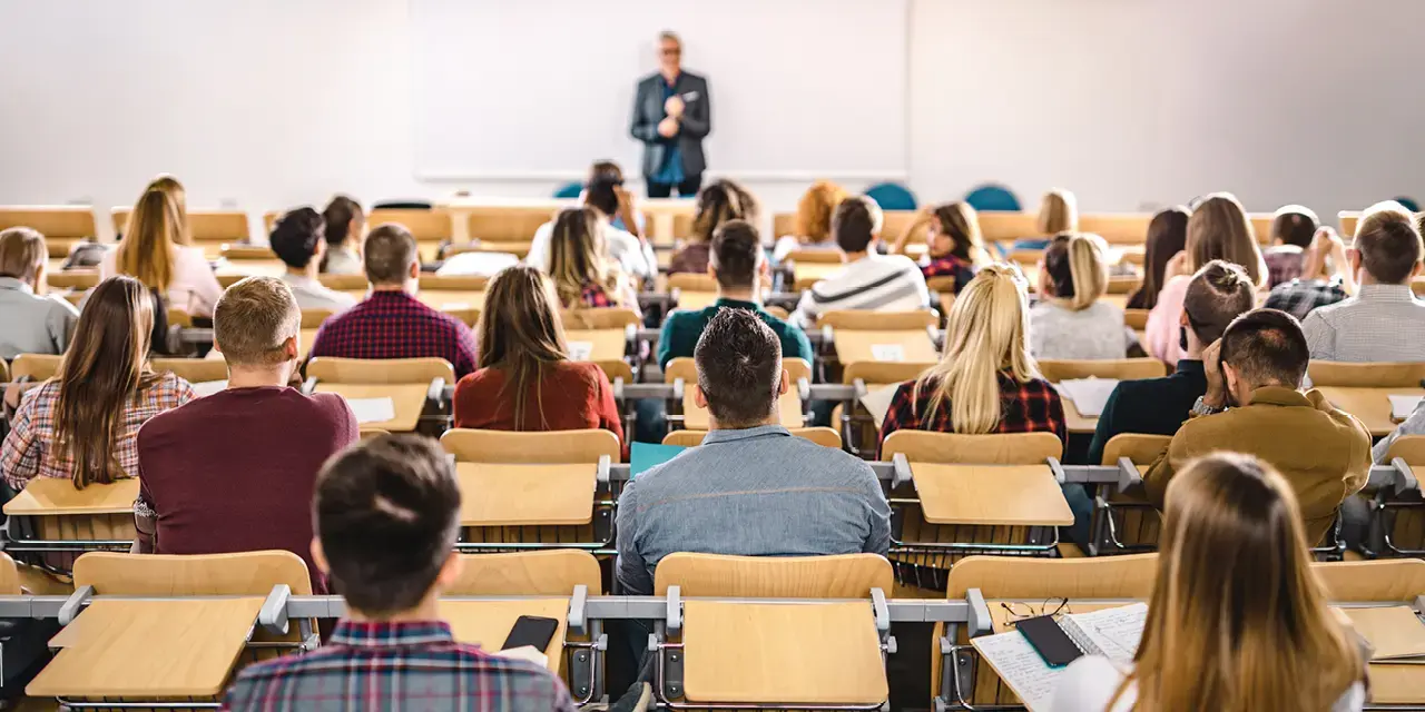 View from behind of students seated in a classroom facing their instructor at the front of the room.