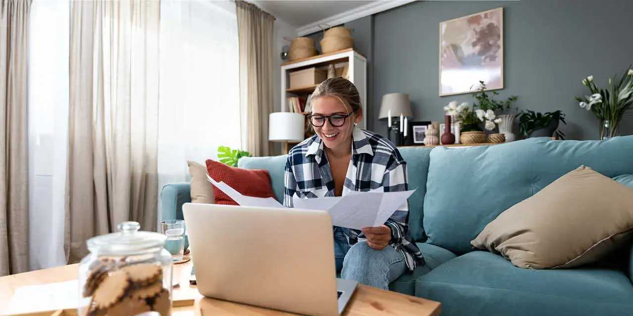 Female student holding papers in her hands and looking at a laptop.