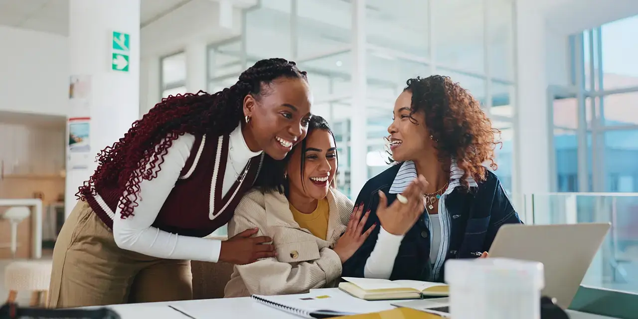 Young professional women looking at a laptop, excited and accomplished. Group of friends with computer, achieving goals in an office setting. 