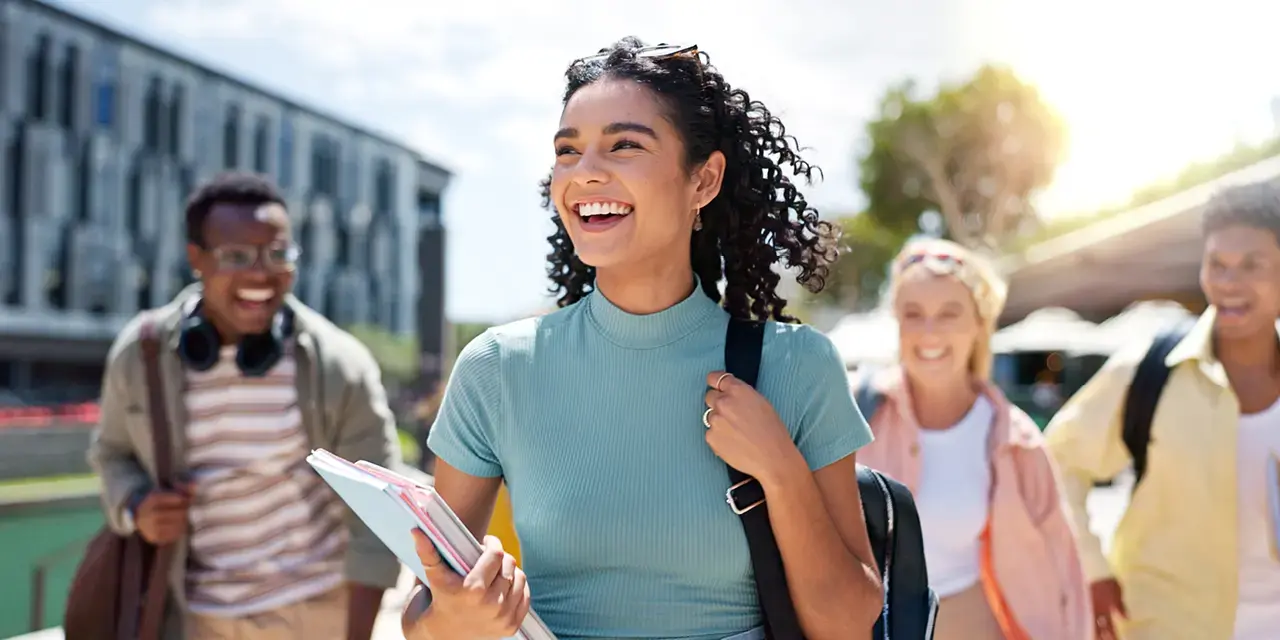 Smiling woman with a backpack over one shoulder and carrying text books.