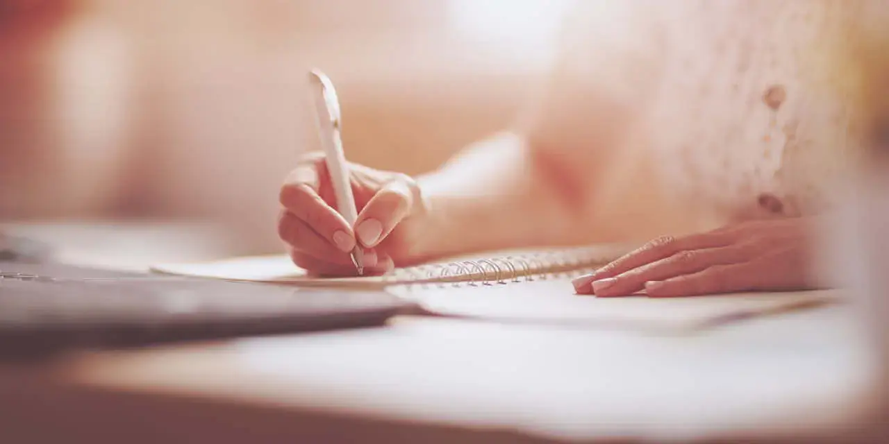 Woman writing in notebook at the office. Close-up panoramic view. Concept of the freelancer and of doing business at home.
