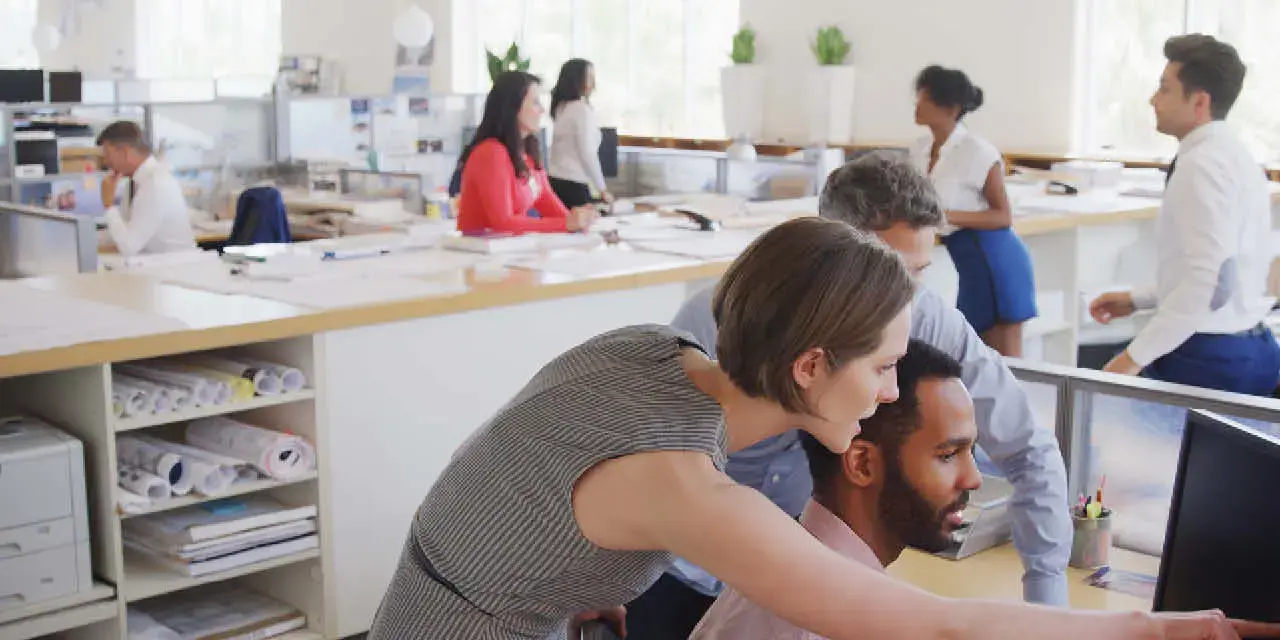 Multi-Cultural Business Team Meeting Around Desk In Modern Open Plan Architects Office Together