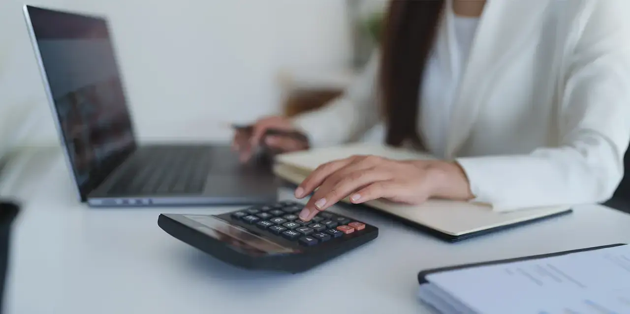 Closeup of person at a desk with a laptop and calculator.