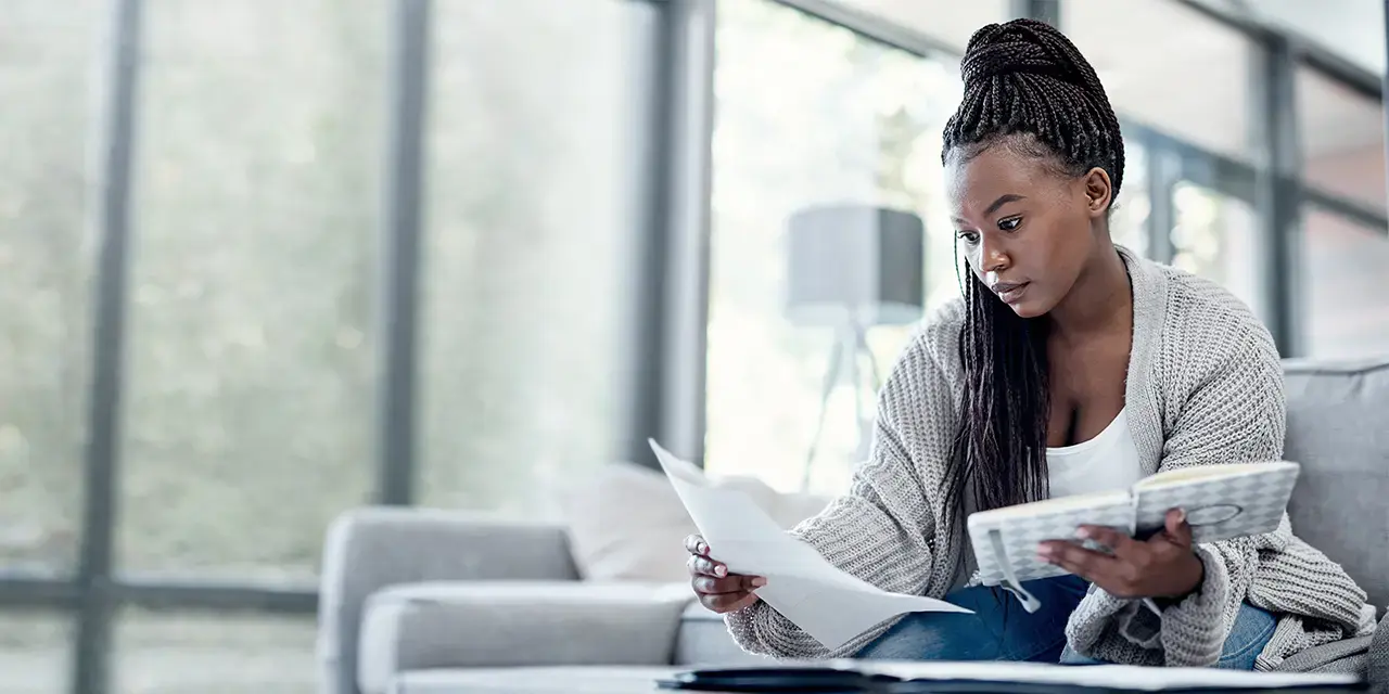  Shot of a young woman going over paperwork on the sofa at home.