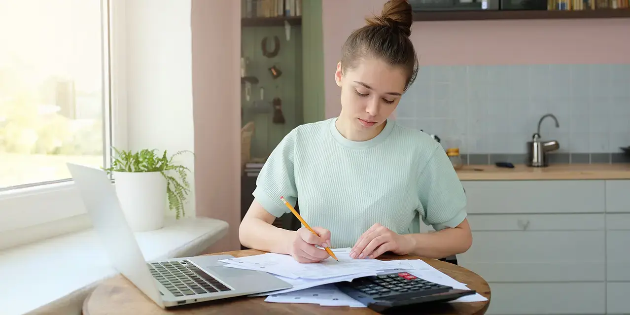 Portrait of young woman, sitting at kitchen table, filling out law school student loan application forms.