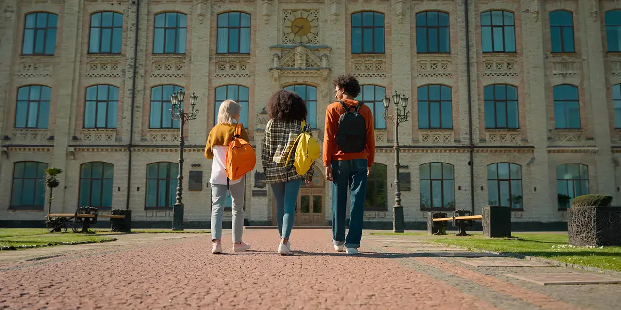 Back view of three people outside walking to class on a university campus. 