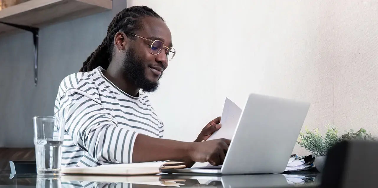 African American male law student working with laptop computer remote while sitting at glass table in living room.