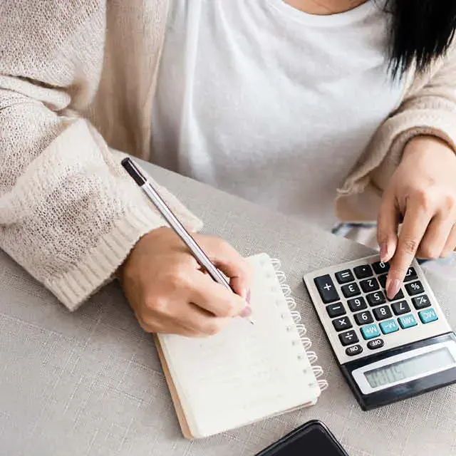 Close up of a one hand on a calculator, and the other hand taking notes in a notebook.