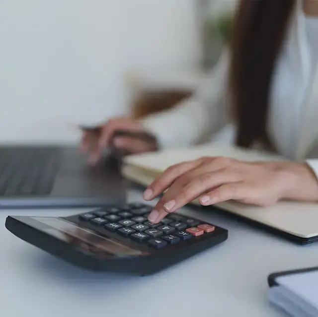 Closeup of person at a desk with a laptop and calculator.