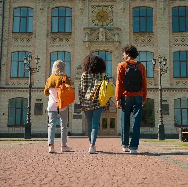 Back view of three people outside walking to class on a university campus. 