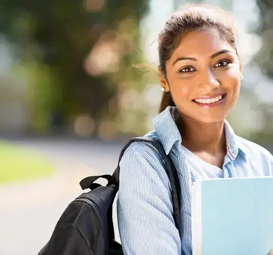 A woman holds her laptop close to her body with the sun shining in the background