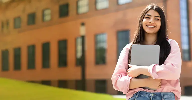 Portrait of happy Hispanic lady student posing with laptop in hands outdoors. 