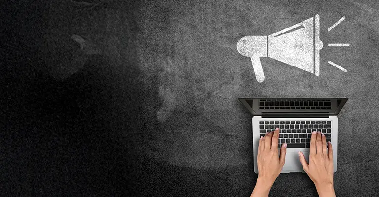 Hands on a laptop with megaphone icon on blackboard 