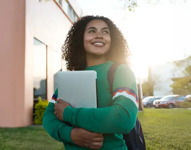 Women walking outside with books in her hands looking into the distance.