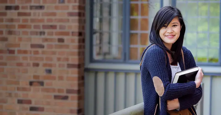 Female wearing a navy-blue sweater holding a notebook close to her chest.