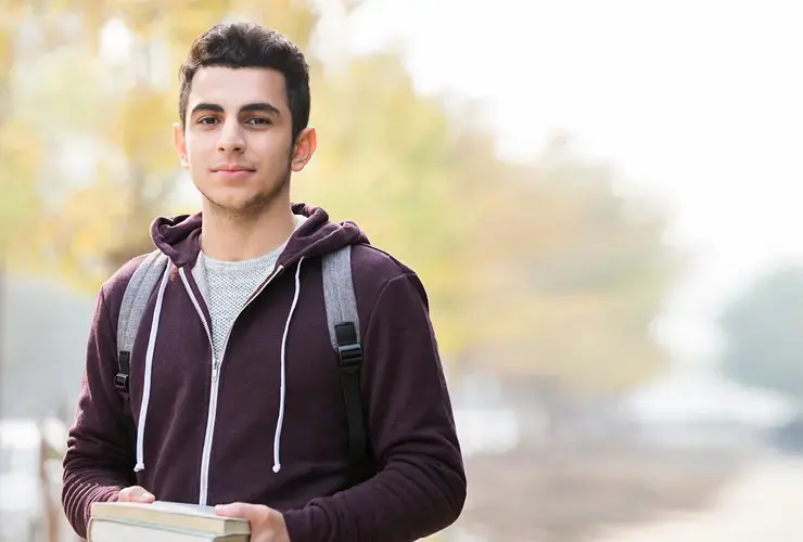 Young man wearing a brown zip-up hoodie and holding books