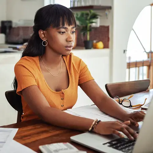 Young woman sittle at a desk with her hands on a laptop.  She is looking at the laptop.