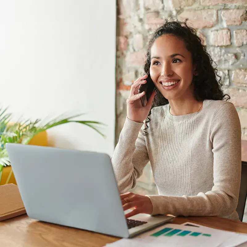 Young woman talking on phone while using laptop at office.