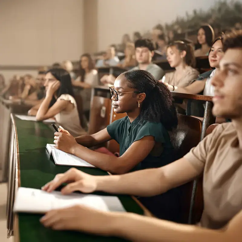 University students seated in a lecture hall. Focus is on a young African American woman who is listening intentively.