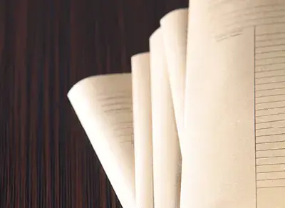 Close-up of open book pages fanned out on a wooden surface, showing printed text and lined sections.