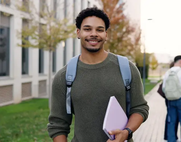 Smiling law student standing on campus path holding a folder. 