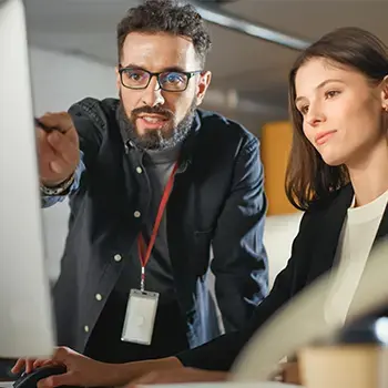 Two people looking at a computer screen. One person is pointing to the screen.