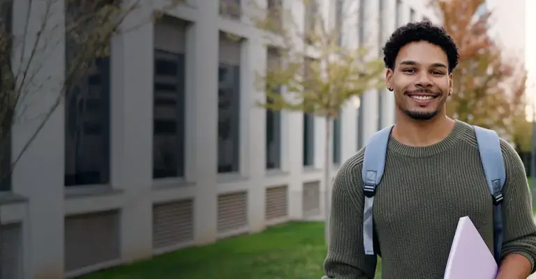 Smiling law student standing on campus path holding a folder. 