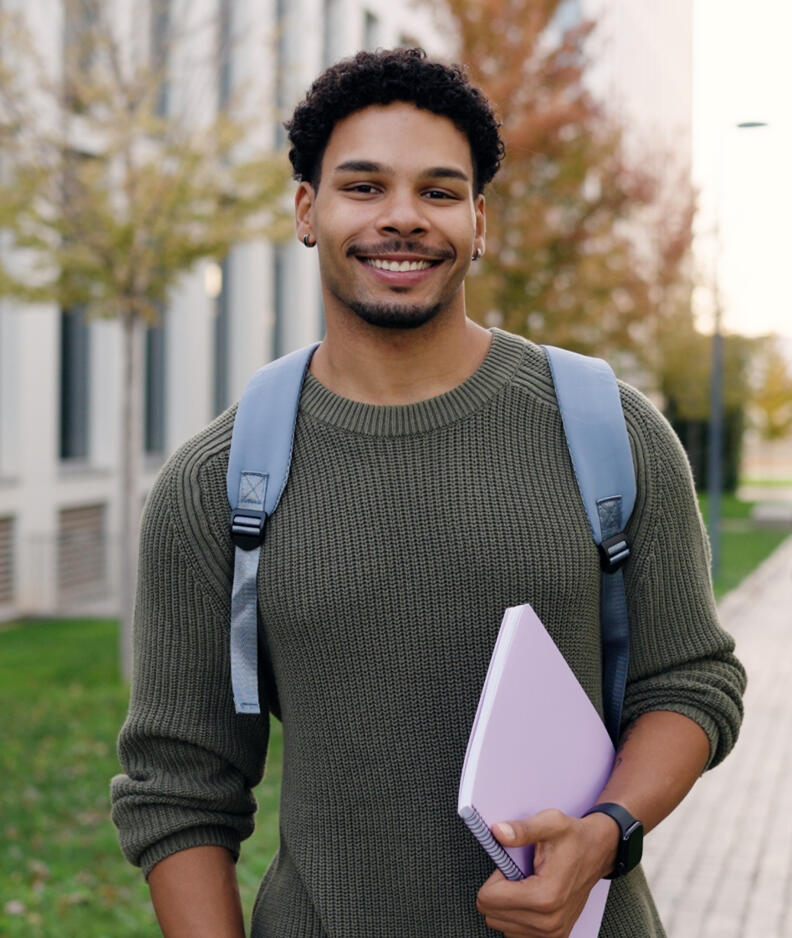Smiling law student standing on campus path holding a folder. 